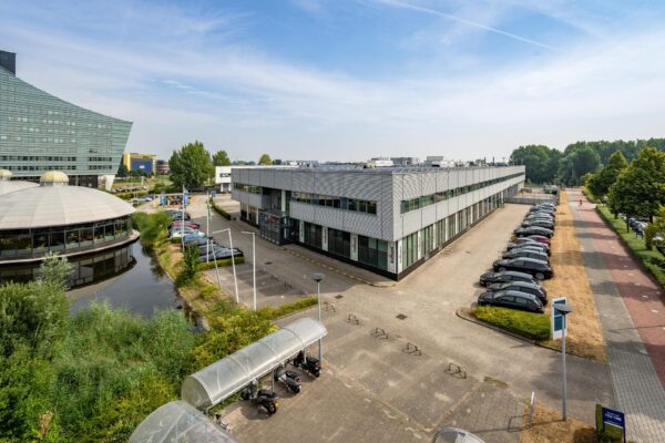Kantoorgebouw aan de Rivium Boulevard met omliggende parkeerplaatsen en fietspad op een zonnige dag.